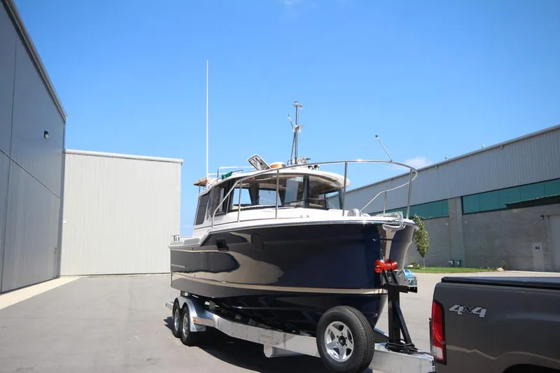 Slide: The Image of 2025 Ranger Tugs R-23 boat on trailer, parked near industrial buildings. - 6