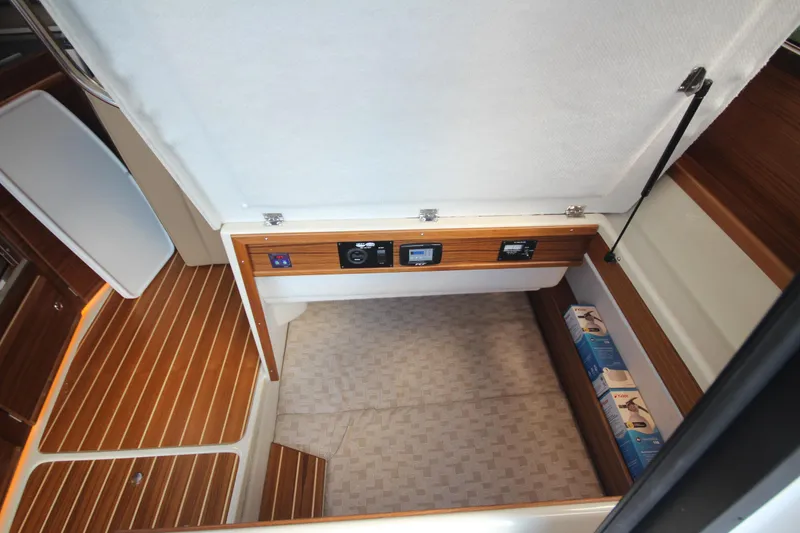 Slide: The Image of 2025 Ranger Tugs R-29 Command Bridge interior storage compartment with wood finish and control panels. - 34