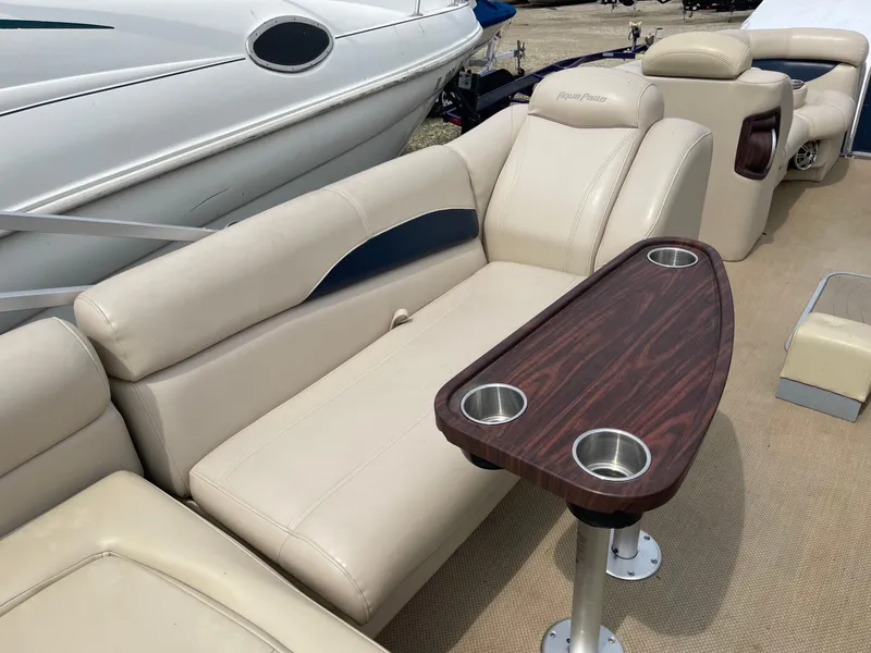 Slide: The Image of 2015 AquaPatio 240EL3 Triple boat interior with beige seating and wooden table. - 10