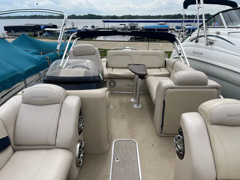 Slide: The Image of 2015 AquaPatio 240EL3 Triple pontoon boat interior with beige seating and lake view. - 4