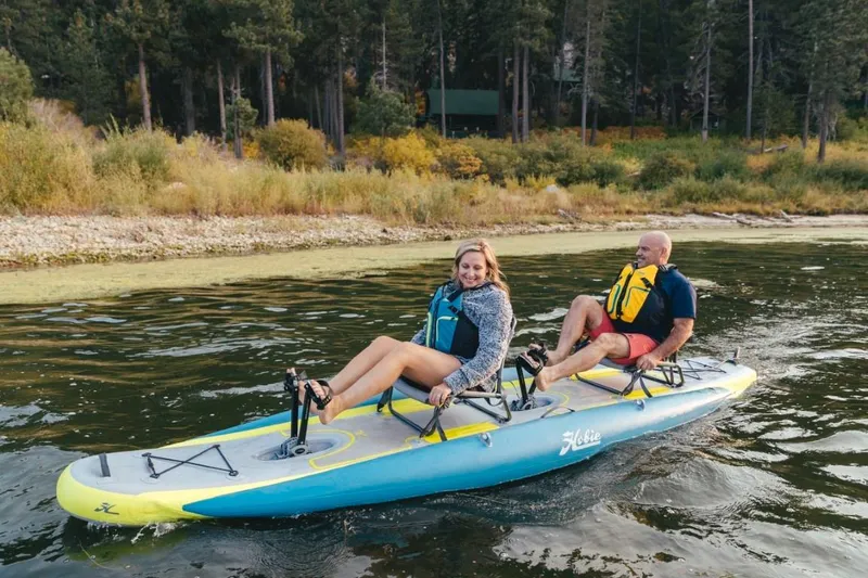 The Image of 2023 Hobie iTrek 14 Duo inflatable kayak with two people pedaling on a lake. - 0