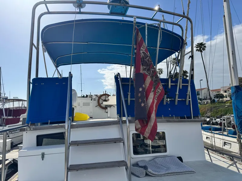 Slide: The Image of 1980 DeFever Trunk Cabin Motoryacht with blue canopy and American flag, docked in marina. - 3