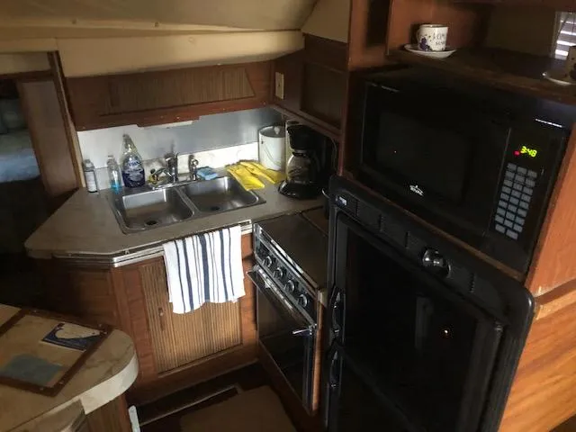 Slide: The Image of 1983 Sea Ray 390 Sport Fisherman kitchen with sink, stove, microwave, and wooden cabinets. - 21