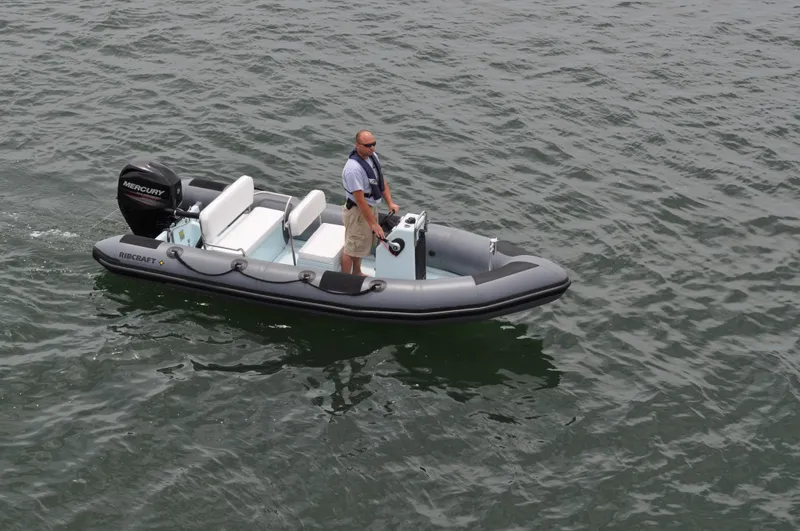Slide: The Image of 2024 Ribcraft 4.8 inflatable boat on water with a person standing at the helm. - 2