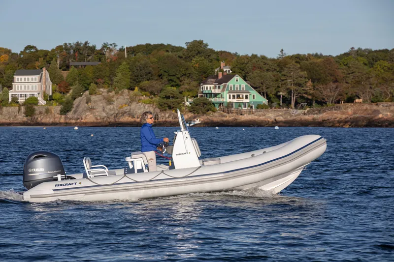 The Image of 2024 Ribcraft 5.85 boat cruising on a scenic lake near shoreline houses. - 0