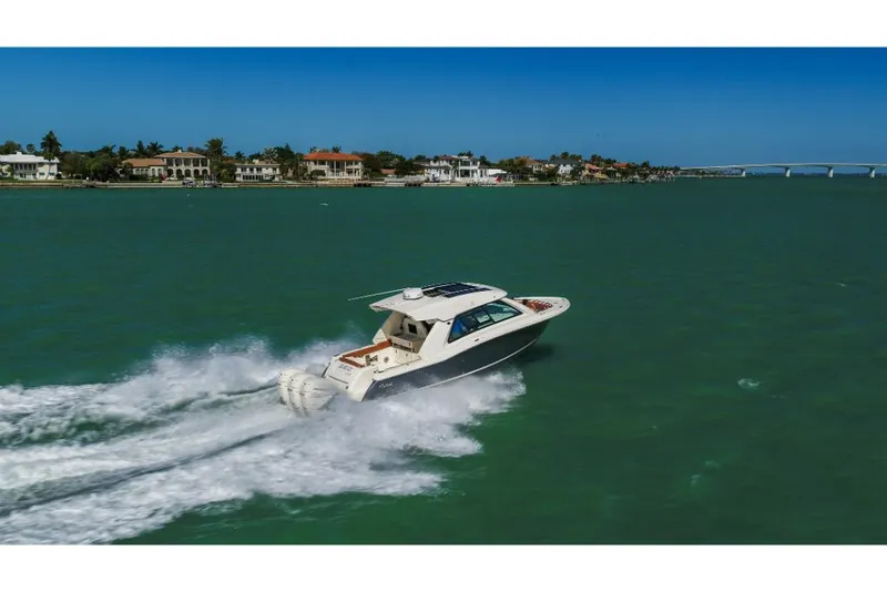Slide: The Image of 2023 Scout 350 LXZ boat cruising on a sunny day near coastal homes. - 15