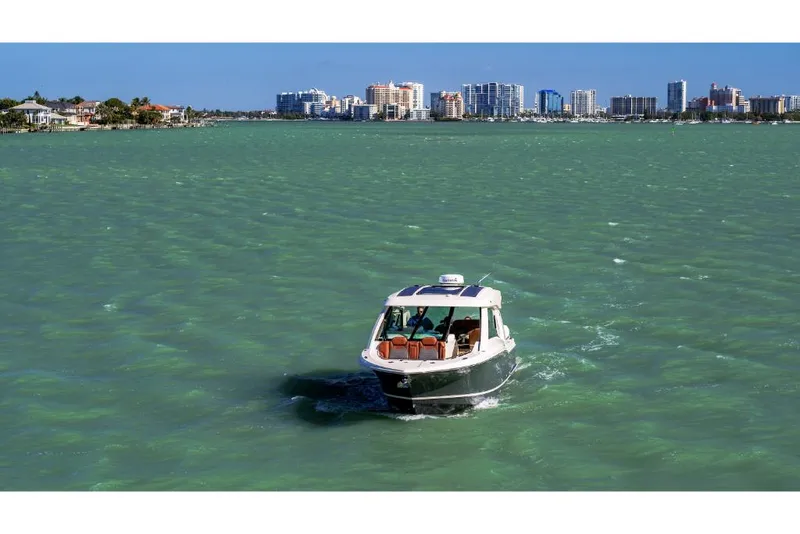 Slide: The Image of 2023 Scout 350 LXZ boat cruising on turquoise waters with city skyline in the background. - 20