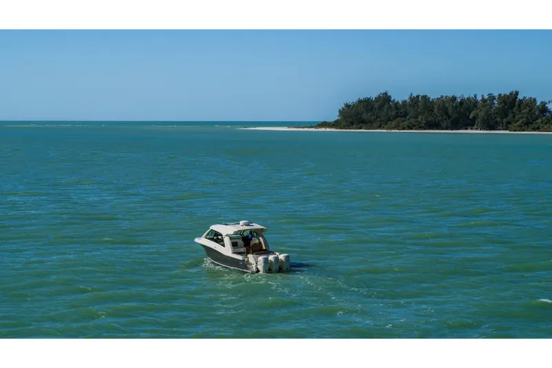 Slide: The Image of 2023 Scout 350 LXZ boat cruising on turquoise waters near a forested island. - 23