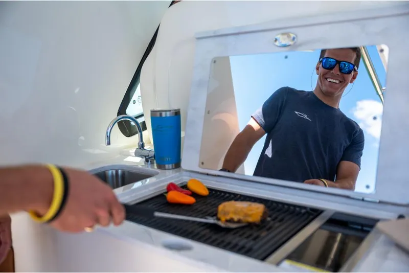 Slide: The Image of Man grilling on a 2023 Scout 350 LXZ boat's outdoor kitchen. - 32