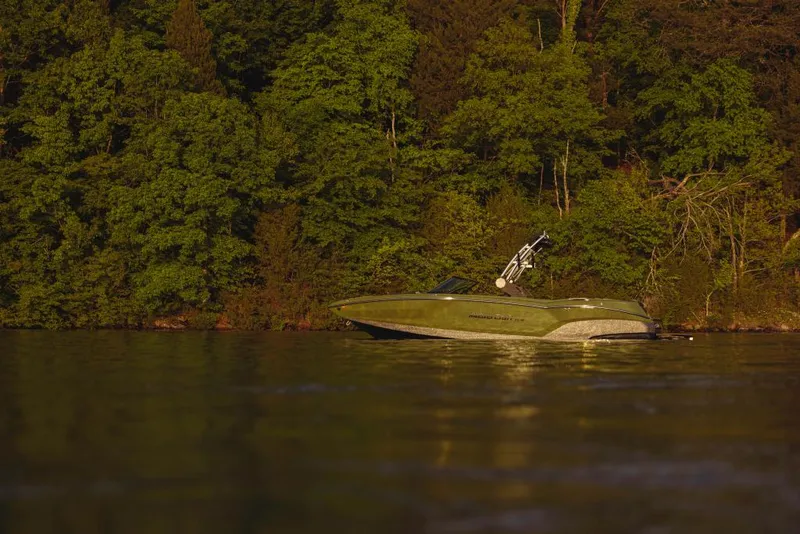Slide: The Image of 2023 MasterCraft NXT24 boat on a calm lake with a forested background. - 10