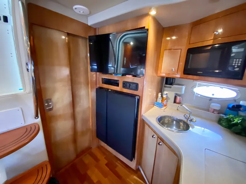 Slide: The Image of 2002 Regal 3860 Commodore yacht interior with kitchenette, TV, and wooden cabinetry. - 24