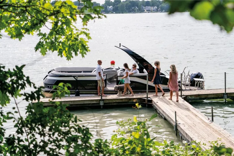 Slide: The Image of People boarding a 2022 Harris Grand Mariner 250 pontoon boat at a lakeside dock. - 7