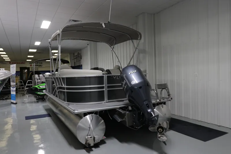 Slide: The Image of 2023 Sylvan Mirage 8522 LZ pontoon boat displayed indoors with canopy and motor. - 2