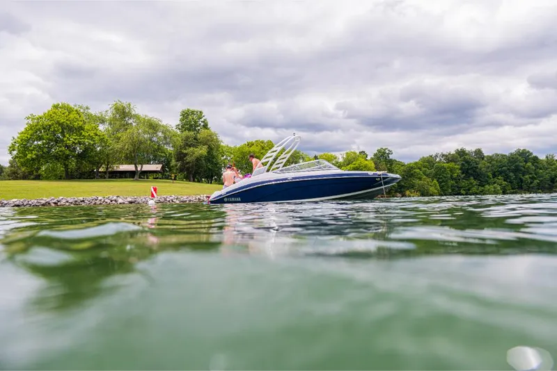 Slide: The Image of 2023 Yamaha Outboards 195S boat on a serene lake near a lush green shoreline. - 12