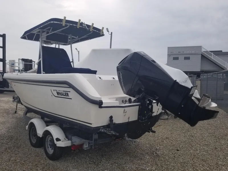 Slide: The Image of 2001 Boston Whaler 23 Outrage boat on trailer, featuring outboard motor and T-top canopy. - 2