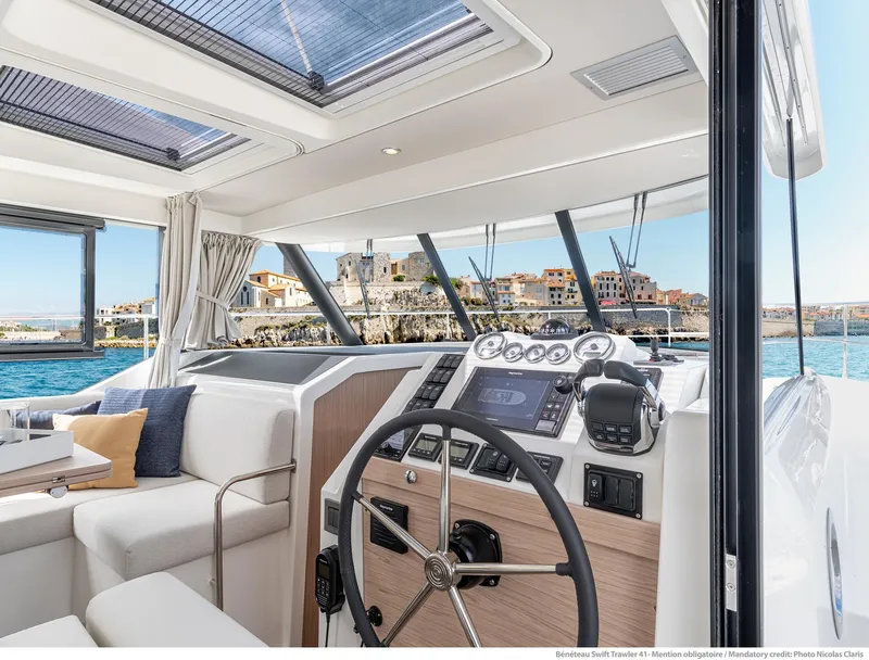 Slide: The Image of 2025 Beneteau Swift Trawler 41 Fly interior with modern helm and coastal view. - 1