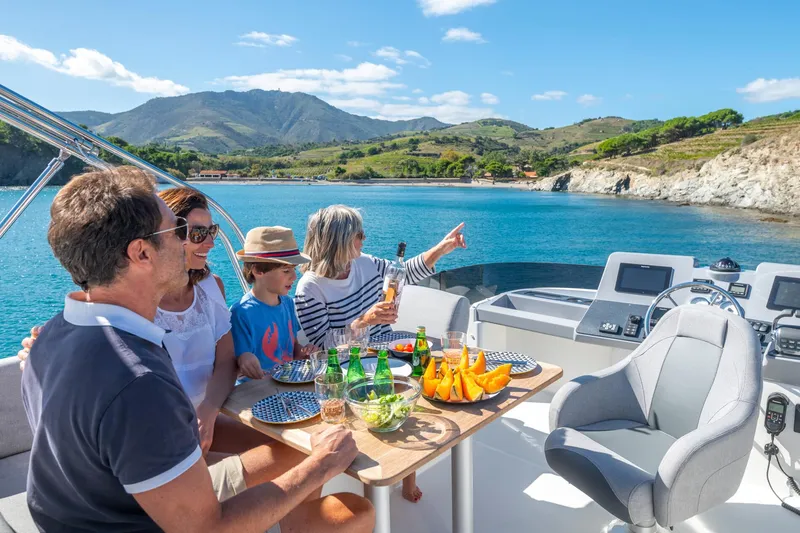 Slide: The Image of Family enjoying a meal on a 2025 Beneteau Swift Trawler 41 Fly, scenic coastal backdrop. - 10