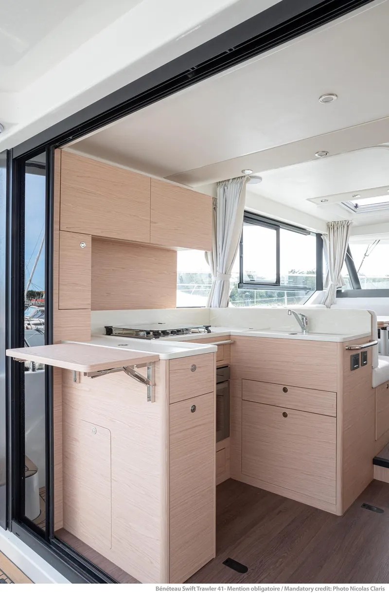 Slide: The Image of 2025 Beneteau Swift Trawler 41 Fly interior, featuring modern kitchen design with light wood cabinetry. - 5