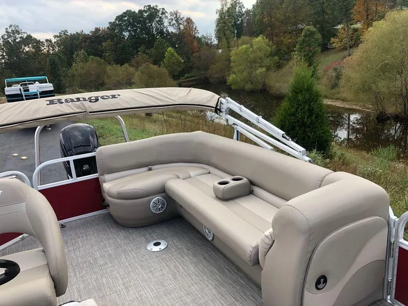Slide: The Image of 2023 Ranger 200C pontoon boat with beige seating, on a scenic lake. - 14