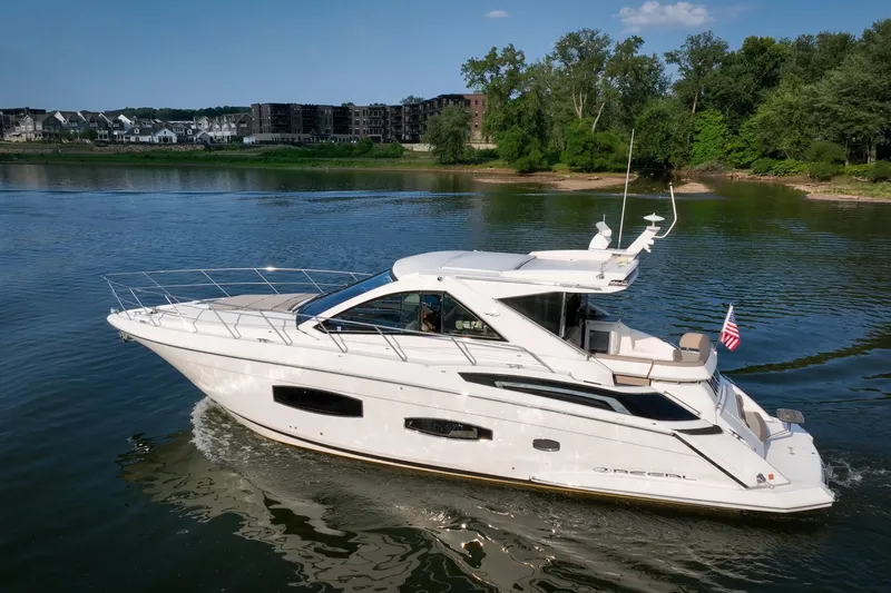 The Image of 2015 Regal 53 Sport Coupe yacht cruising on a serene lake with lush greenery. - 0