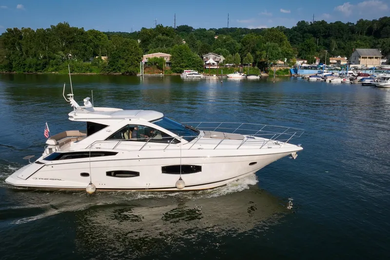 Slide: The Image of 2015 Regal 53 Sport Coupe yacht cruising on a scenic lake with lush greenery. - 18