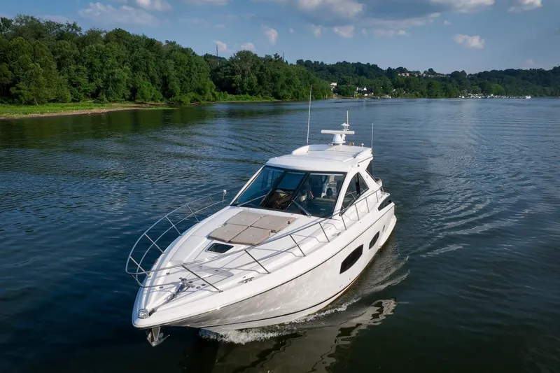 Slide: The Image of 2015 Regal 53 Sport Coupe cruising on a serene lake with lush green shoreline. - 2