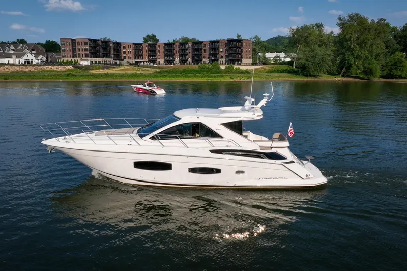 Slide: The Image of 2015 Regal 53 Sport Coupe yacht cruising on a serene river with scenic backdrop. - 7