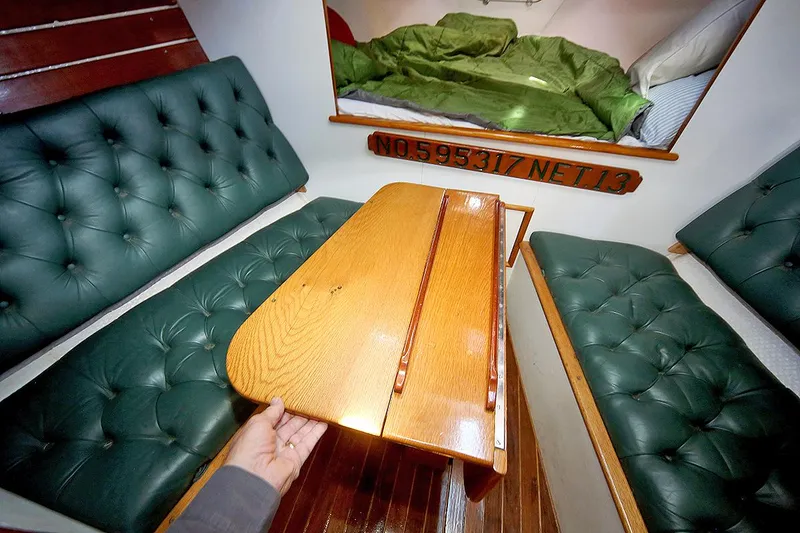 Slide: The Image of Interior of 1979 Custom Van Dyne Schooner with green cushioned seating and wooden table. - 43