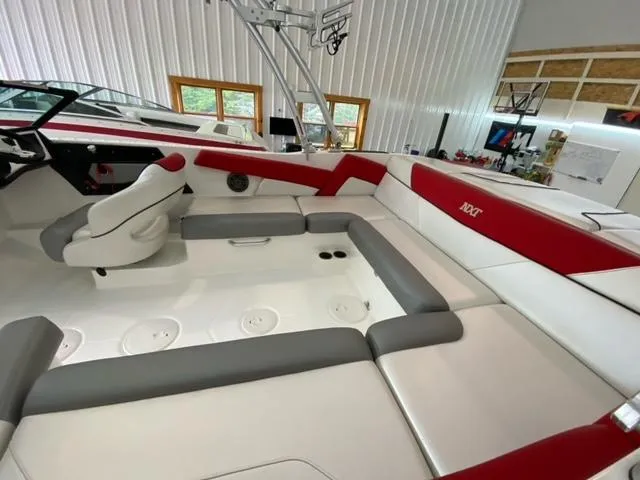 Slide: The Image of 2017 MasterCraft NXT22 boat interior with red and gray seating in a spacious garage. - 2