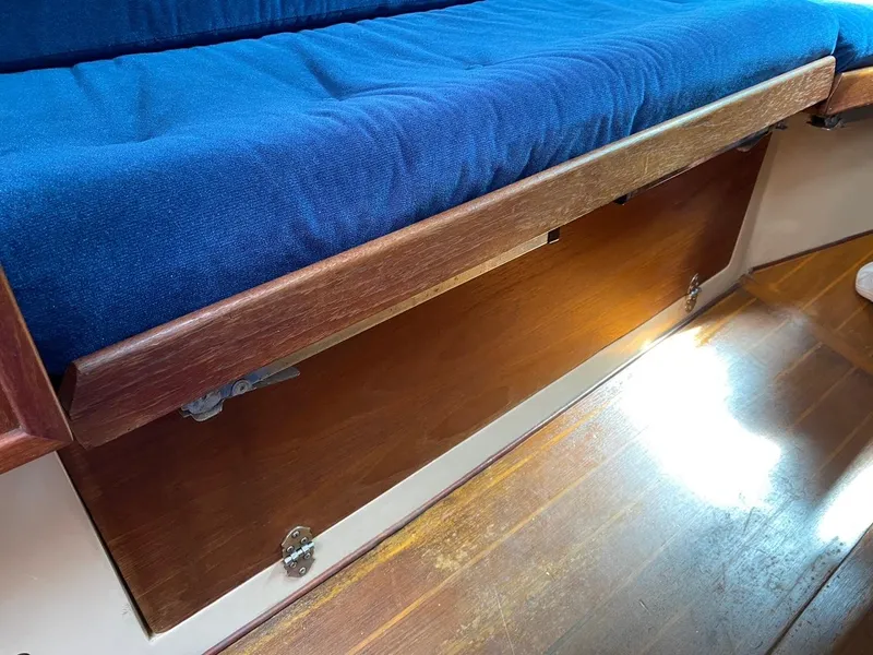 Slide: The Image of Interior of 1988 Newport 27 sailboat with blue cushioned seating and wooden storage. - 12