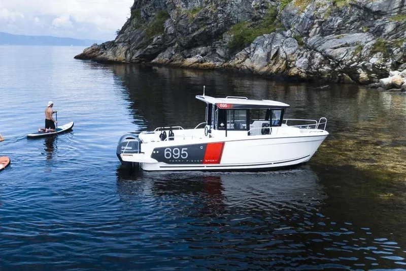 Slide: The Image of 2026 Jeanneau NC Sport 695 Series 2 boat near rocky shoreline with paddleboarders. - 2