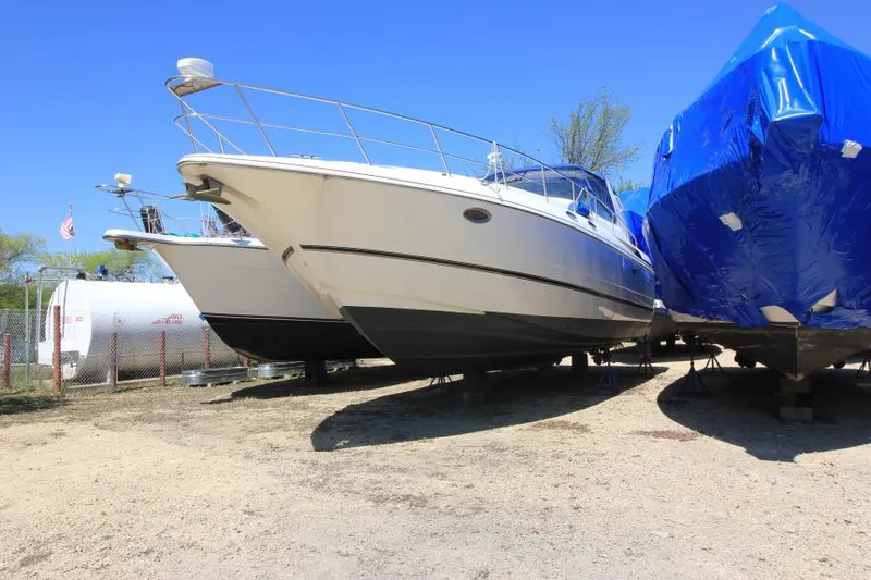 Slide: The Image of 2000 Cruisers Yachts 3870 Express boat on dry dock, alongside a blue-covered vessel. - 4