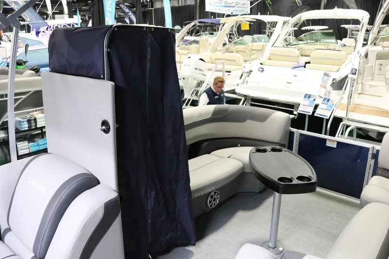 Slide: The Image of 2023 Sylvan L3 ENT pontoon boat interior with seating and table at a boat show. - 27