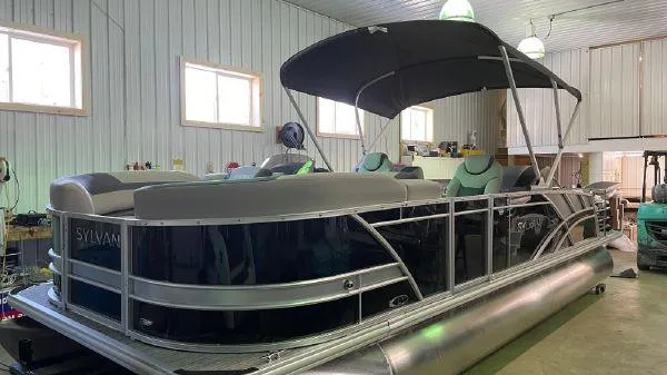 Slide: The Image of 2023 Sylvan L3 RLZ pontoon boat in a warehouse, featuring a sleek design and canopy. - 0
