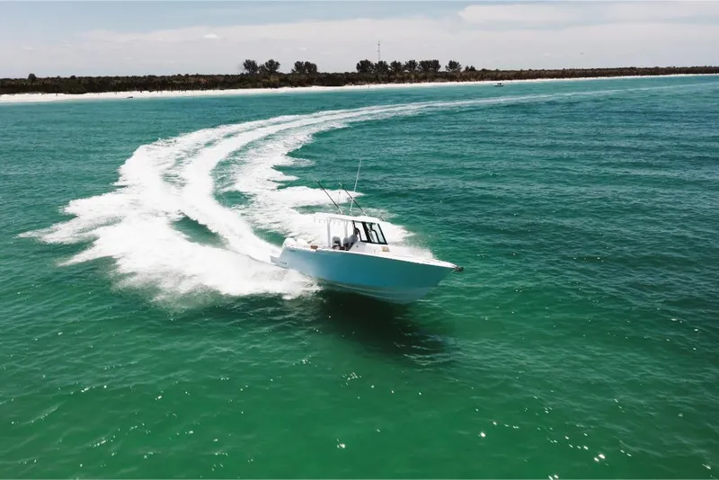 Slide: The Image of 2023 Bertram 28CC boat cruising on turquoise waters near a sandy shoreline. - 12