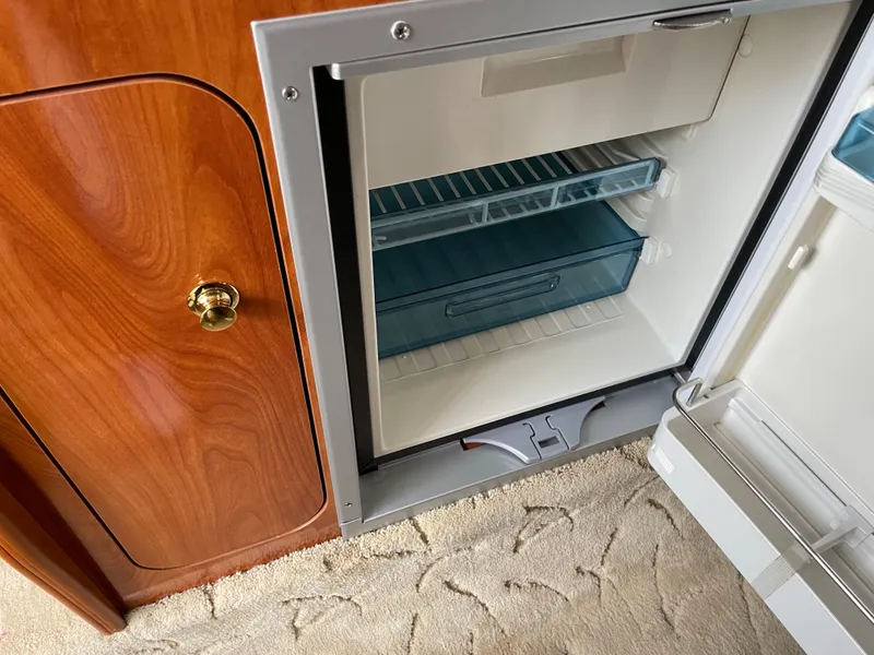Slide: The Image of 2005 Rinker 250 Fiesta Vee interior with open mini fridge and wooden cabinet. - 15