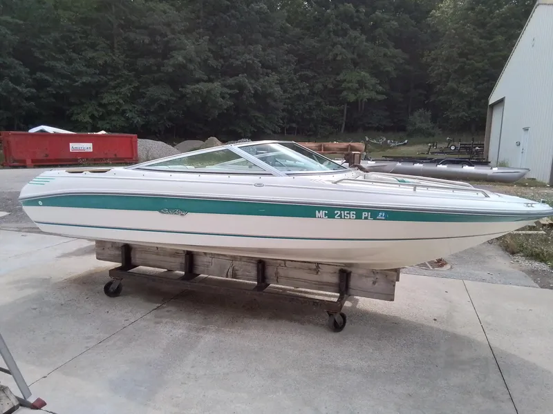 The Image of 1993 Sea Ray 180 BR boat on trailer, parked outdoors near trees and building. - 1