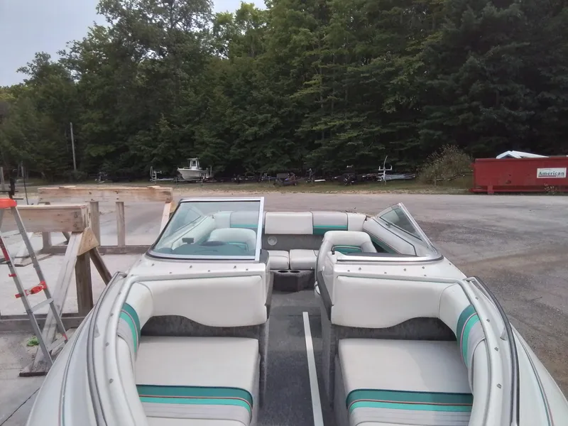 Slide: The Image of 1993 Sea Ray 180 BR boat with white and teal interior, parked near a forested area. - 3