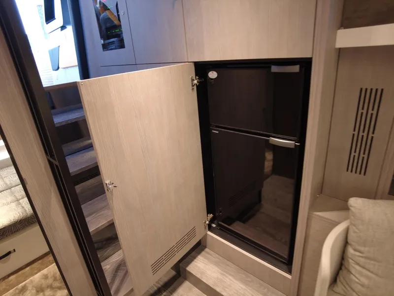 Slide: The Image of 2023 Cranchi A46 yacht interior with open cabinet revealing a black refrigerator. - 33
