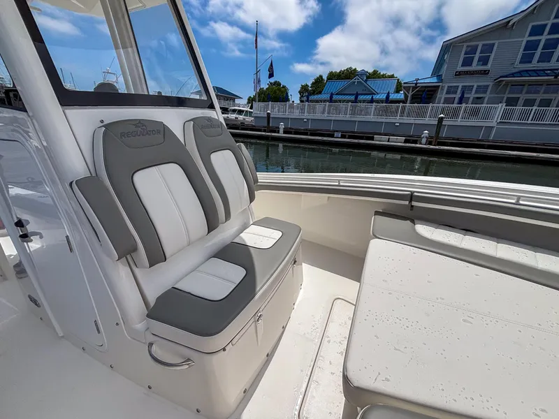 Slide: The Image of 2025 Regulator 23 boat interior with cushioned seating, dockside view, and blue sky. - 22