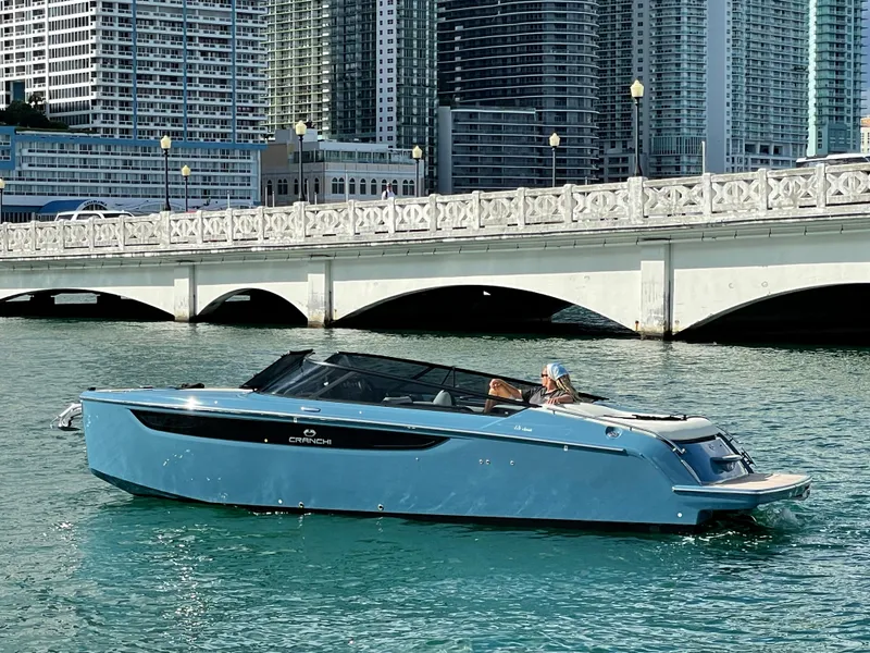 Slide: The Image of 2022 Cranchi 26 Classic boat cruising near a bridge in a cityscape. - 2