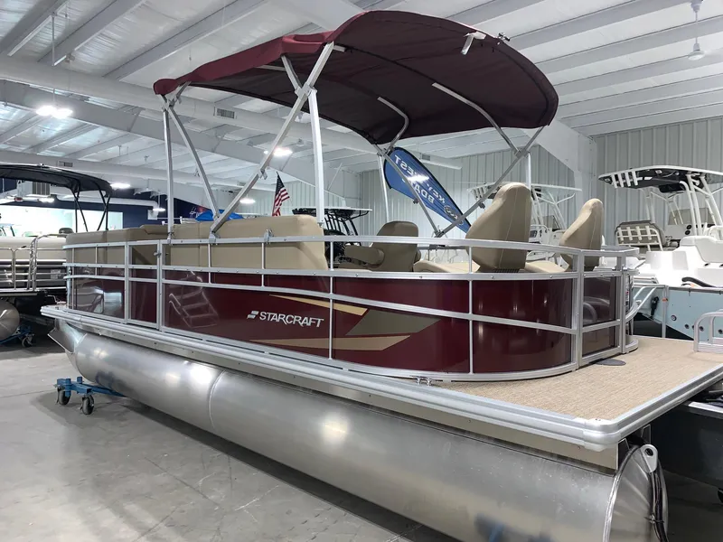 Slide: The Image of 2024 Starcraft LX22 F pontoon boat with maroon exterior and canopy in showroom. - 2