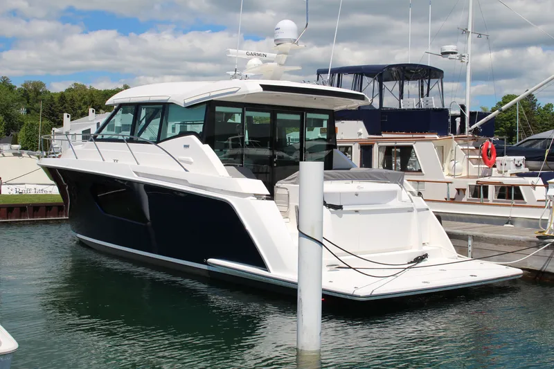 Slide: The Image of 2020 Tiara Yachts C49 Coupe docked in a marina under a partly cloudy sky. - 2