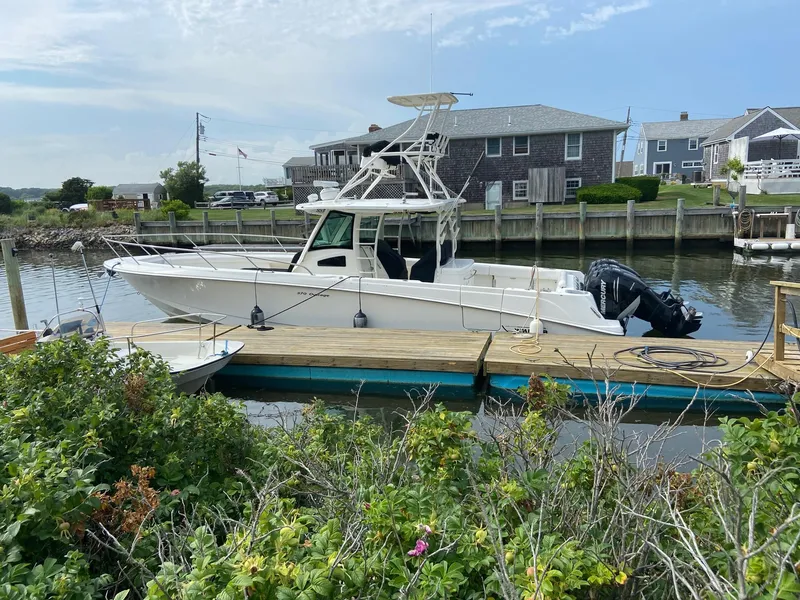 The Image of 2014 Boston Whaler 370 Outrage docked at a marina, surrounded by greenery and waterfront homes. - 0