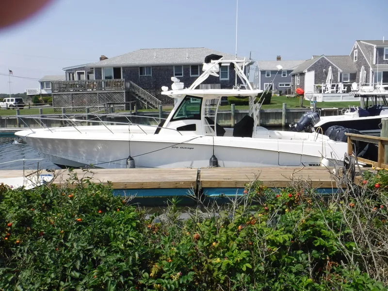 Slide: The Image of 2014 Boston Whaler 370 Outrage docked near coastal homes, surrounded by greenery. - 2