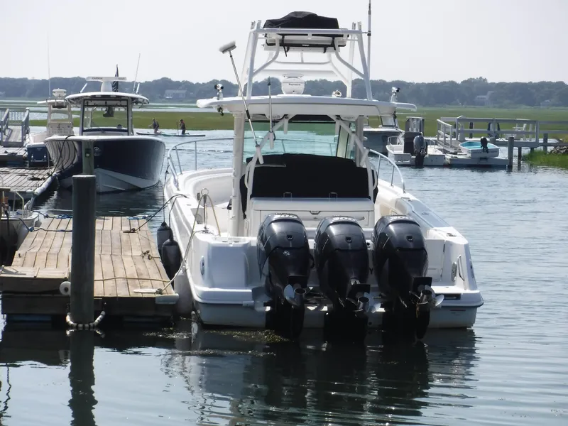 Slide: The Image of 2014 Boston Whaler 370 Outrage docked, featuring triple outboard engines, in a serene marina setting. - 6
