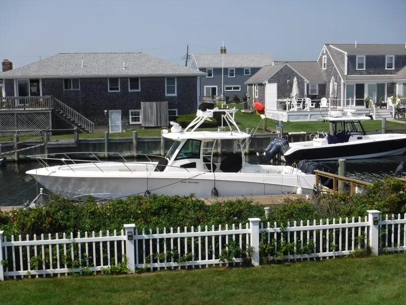 Slide: The Image of 2014 Boston Whaler 370 Outrage docked near coastal homes, surrounded by greenery and white fence. - 8