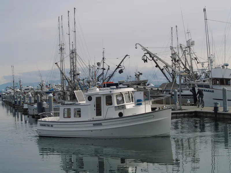 Slide: The Image of Nordic Tug 26 (2025) in a busy marina with fishing boats. - 1