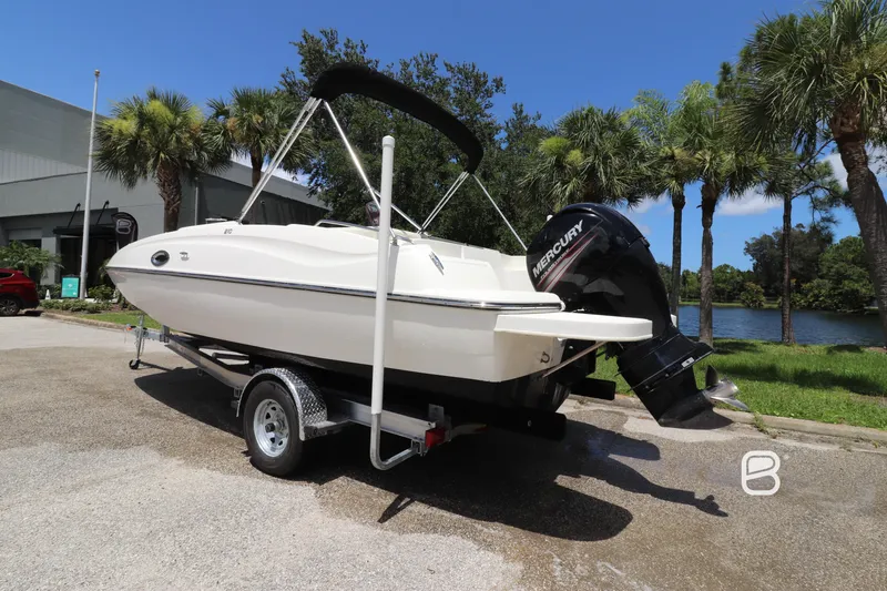 Slide: The Image of 2018 Bayliner 210 DB boat on trailer, parked near palm trees and water. - 6