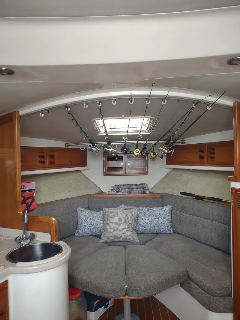 Slide: The Image of 1998 Cabo 31 Express cabin interior with fishing rods, cozy seating, and wooden cabinetry. - 21